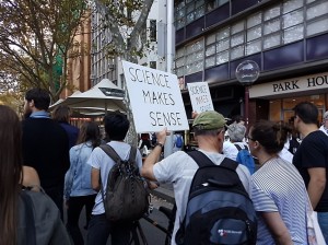 Protesters march down the street. A White man is seen in the foreground, holding a sign that reads 
